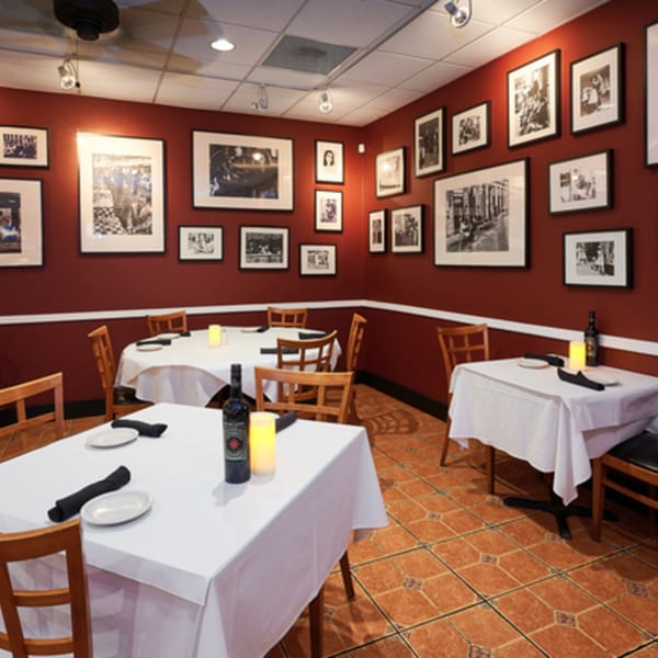 Dining room with red walls adorned with framed black and white photos, set tables, and tiled floors.