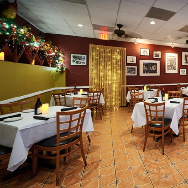 Restaurant dining room with white-clothed tables, wooden chairs, and festive holiday decorations.
