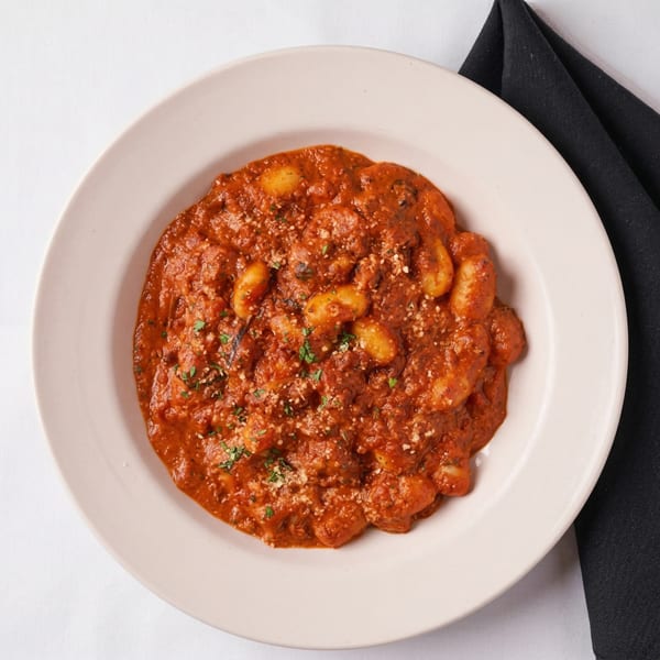 A white bowl filled with gnocchi in a rich red sauce, topped with cheese and herbs.