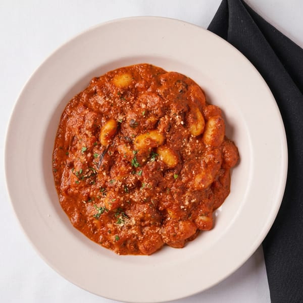 Gnocchi pasta in a rich red sauce, topped with grated cheese and fresh herbs, served on a white plate.