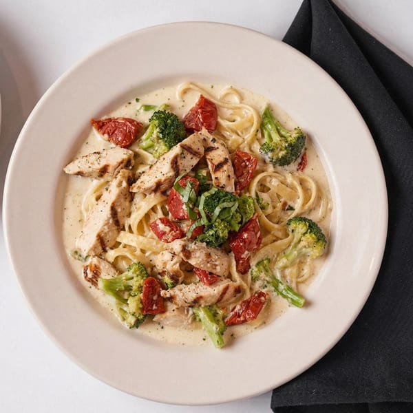 Creamy fettuccine pasta with grilled chicken, sun-dried tomatoes, broccoli, and fresh basil.