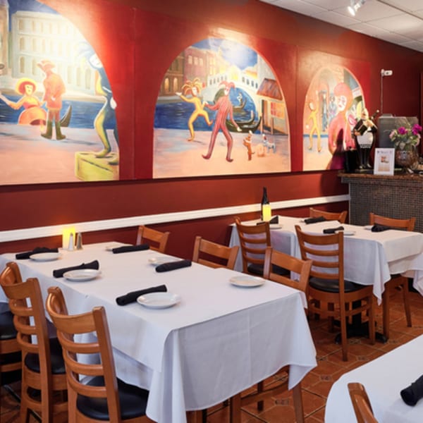 Restaurant dining room with white-clothed tables, wooden chairs, and a large mural depicting Venetian scenes.