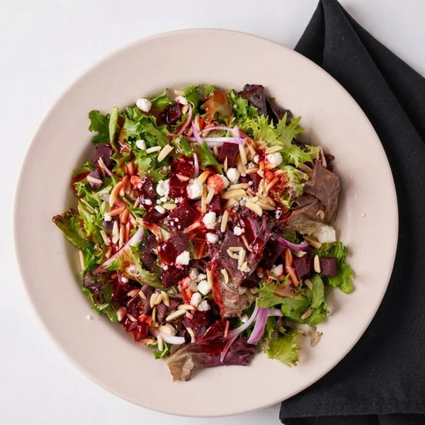 A vibrant salad with mixed greens, beets, goat cheese, sliced almonds, and red onion, drizzled with dressing.